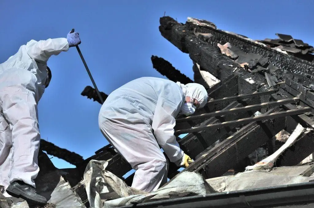 Two workers in protective suits clearing a burned roof structure