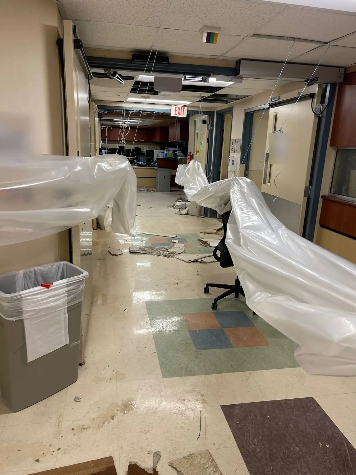 A hospital corridor with plastic containment sheeting hanging from the ceiling and fallen ceiling tiles on the floor