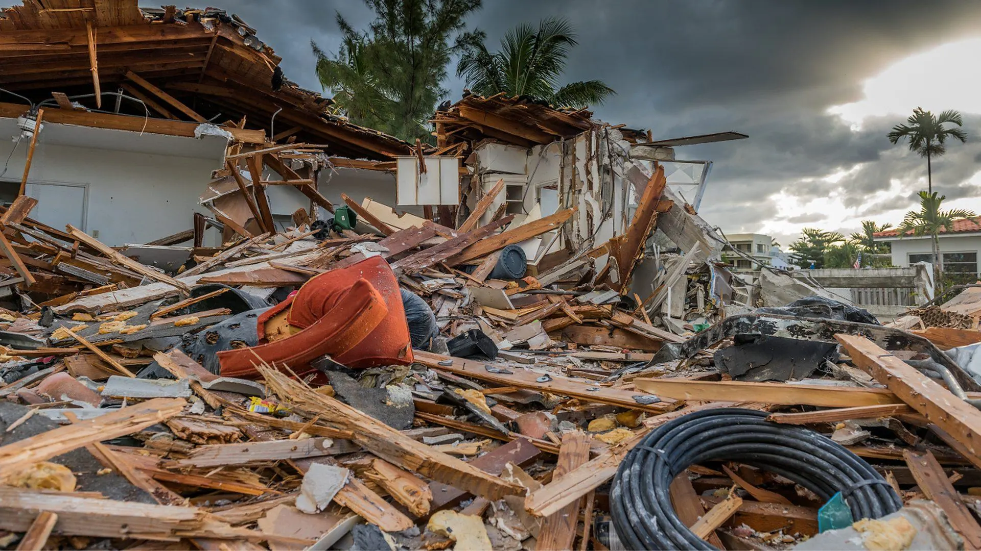 A house destroyed by a storm, with roof beams, lumber and debris piled in the foreground under dark clouds