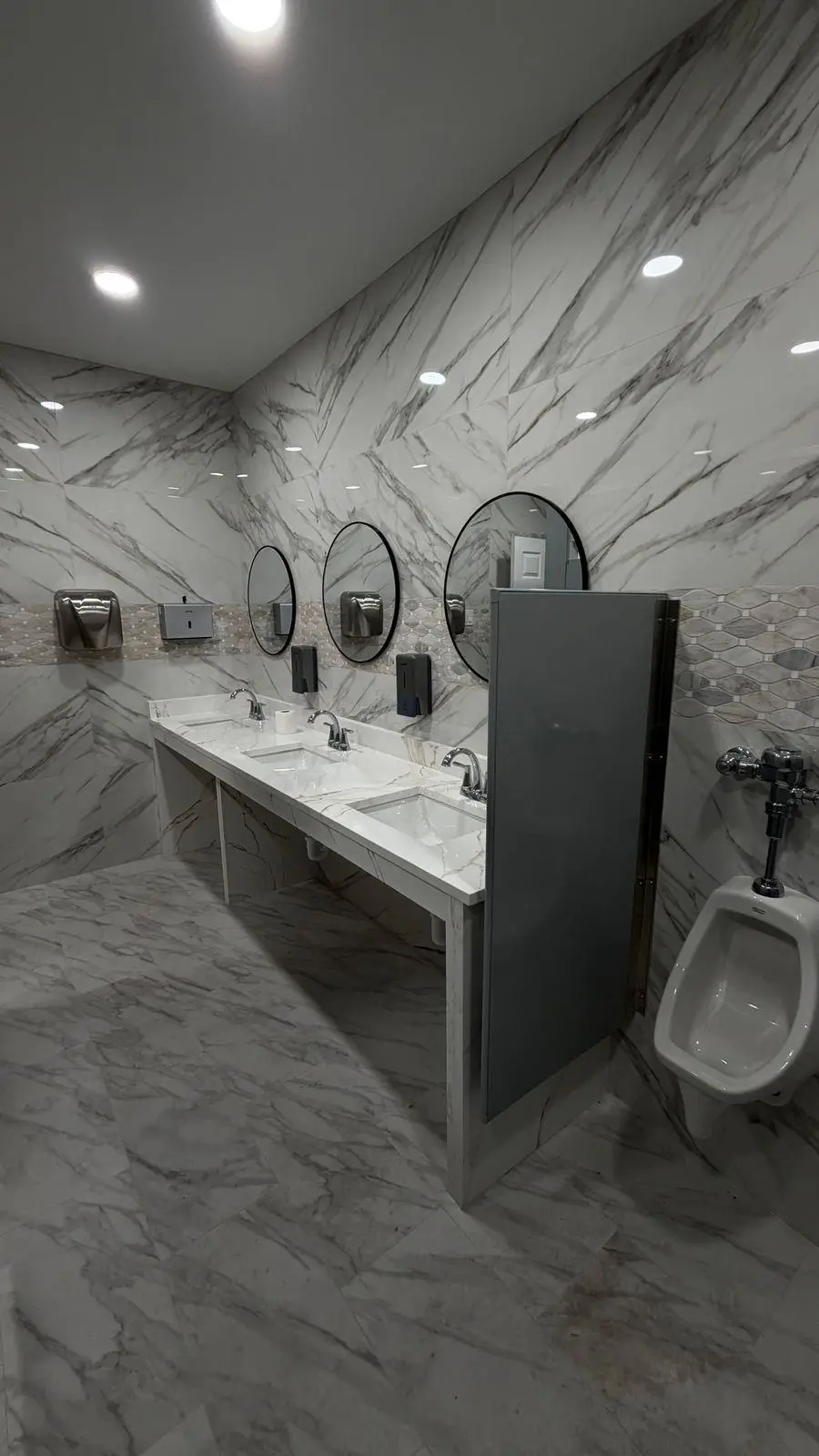 Restroom with marble-look tile, round mirrors, a long vanity and a urinal