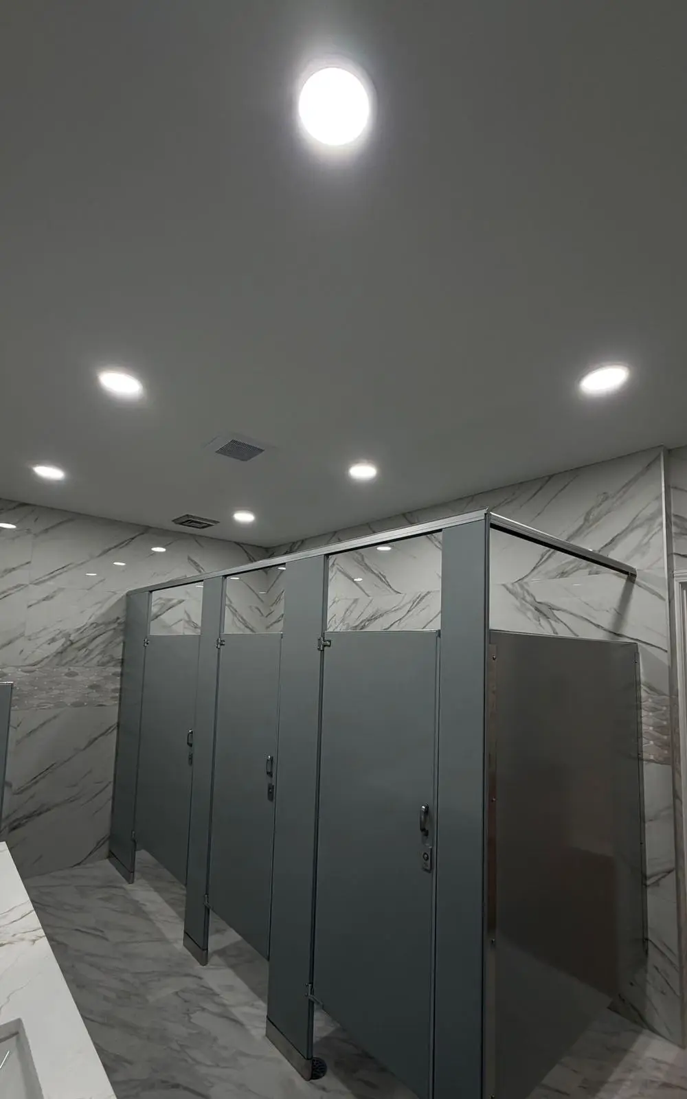 Restroom with marble-look wall tile, gray partitions and recessed lighting