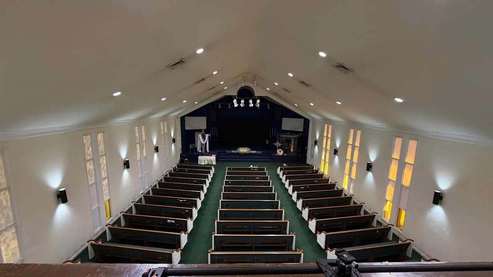 Finished sanctuary seen from the balcony, with rows of pews and a lit stage