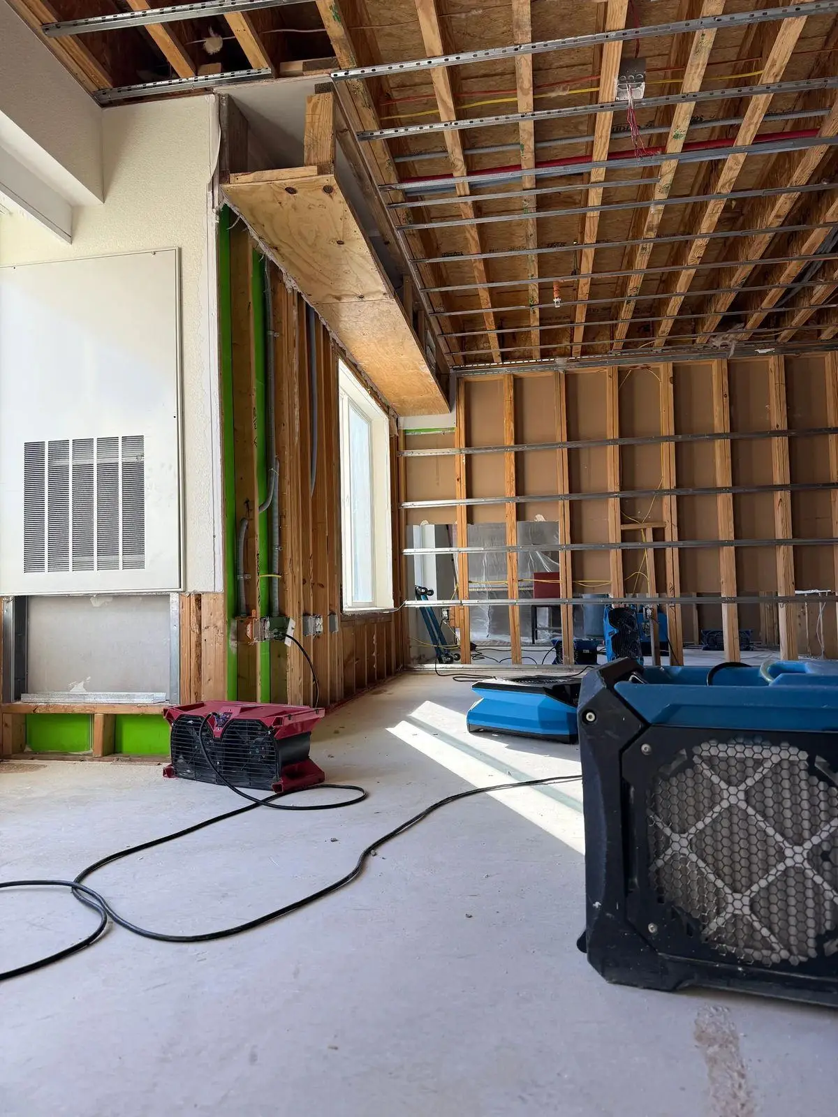 Water-damaged ceiling opened up above a large room, with an air scrubber and drying equipment on the floor